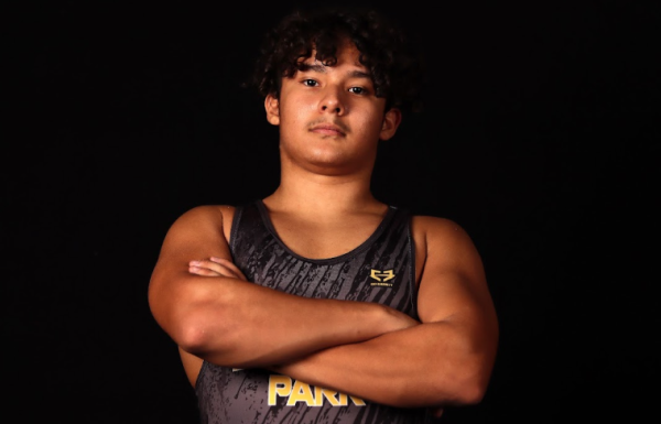 Zach Molina in his wrestling attire with his arms crossed. He has a serious expression on his face as his picture is taken.